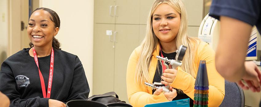 Student holds instrument while other student is smiling at desks.